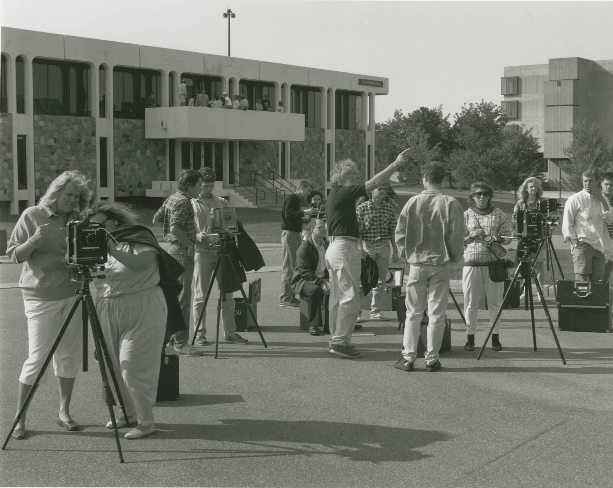 Students and faculty taking photos with cameras on tripods in front of Lake Superior Hall on a sunny day.